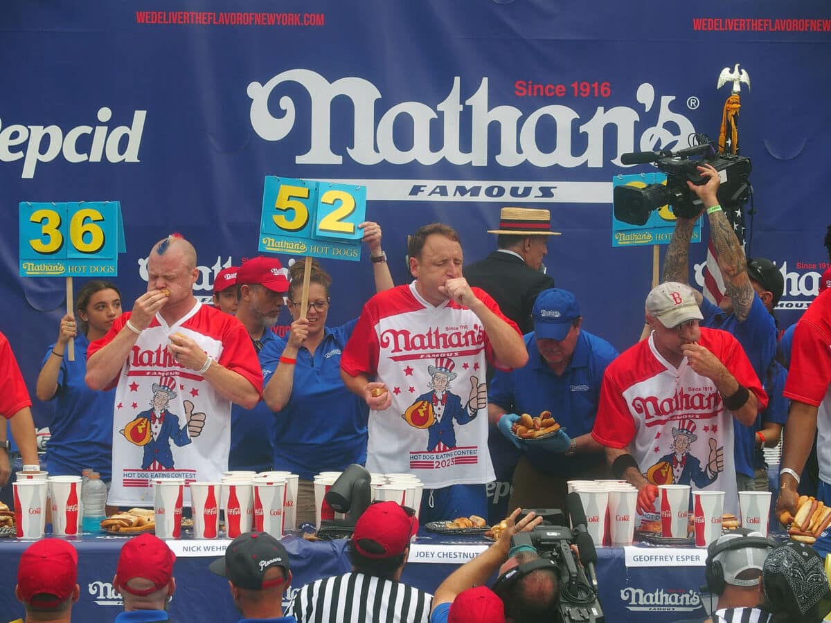 NEW YORK, NY - JULY 04:  Defending champion Joey Chestnut (C) competes in the 2023 Nathan's Famous International Hot Dog Eating Contest at Coney Island on July 4, 2023 in New York City.