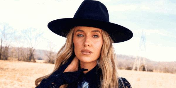 Lainey Wilson poses in a field in a black hat and outfit for her Whirlwind Deluxe album
